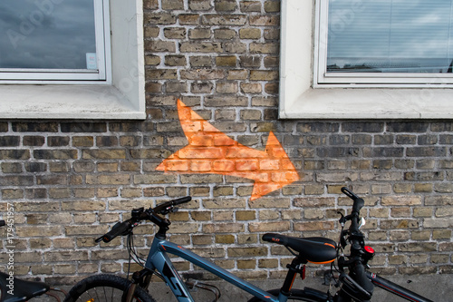 Orange arrow on the wall bettween two windows and a bike photo