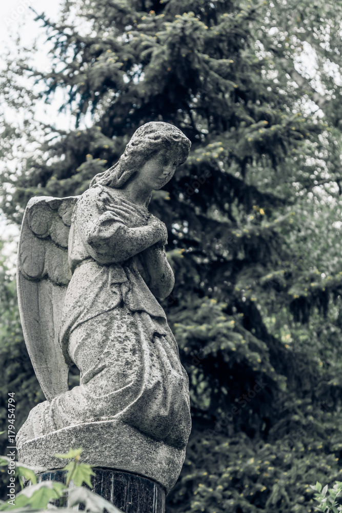 Stone Angel on his knees in the old cemetery - vintage toning