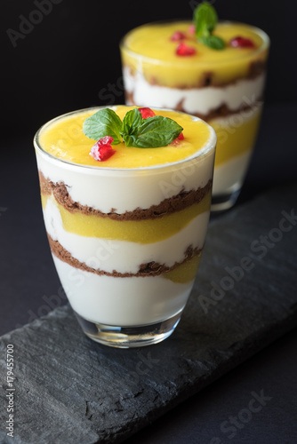 Dessert with mango, yogurt, cookies, decorated with mint leaves and pomegranate seeds.