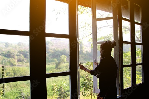 The woman is opening the window to breathe fresh air behind her home.