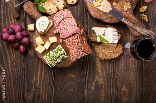 Assorted cheeses on wooden boards plate, grapes, bread wine and pate on dark wooden background, top view, flat lay, copy space.
