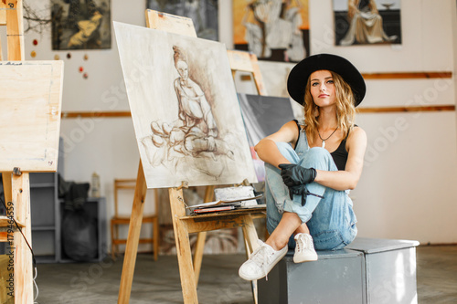 Female artist wears black hat posing near picture indoor the studio