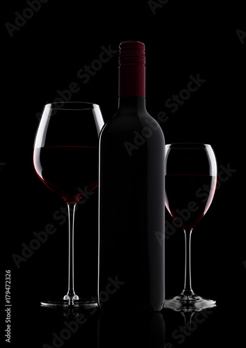 Glass of red wine with bottle with shape on black