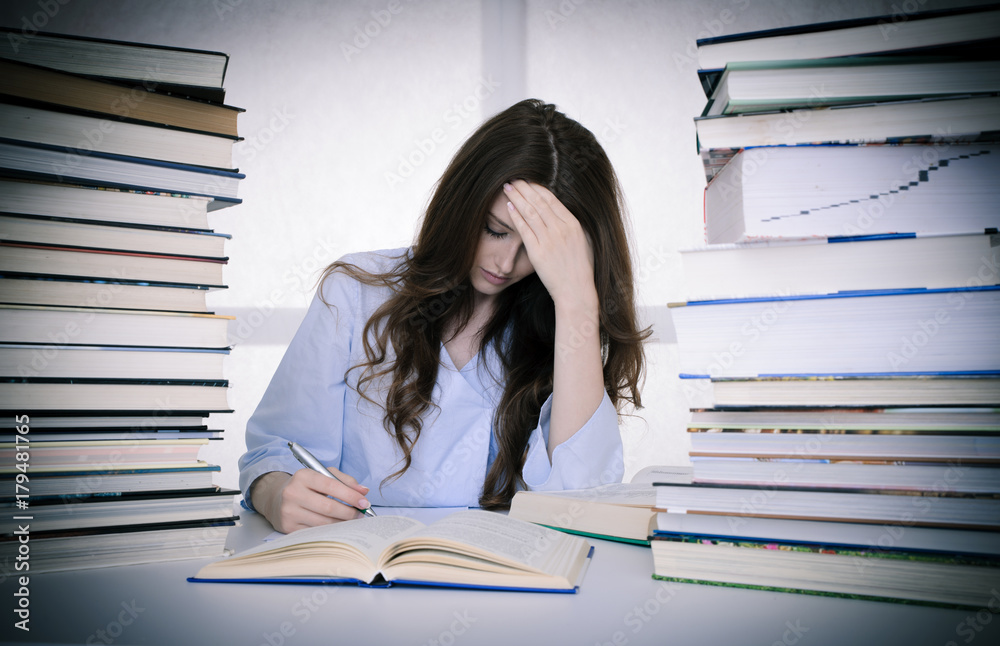 attractive young woman studies wtih hugr book piles on her desk attractive young woman studies wtih hugr book piles on her desk