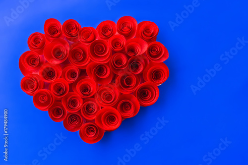 Red roses made of heart-shaped paper on a blue background.