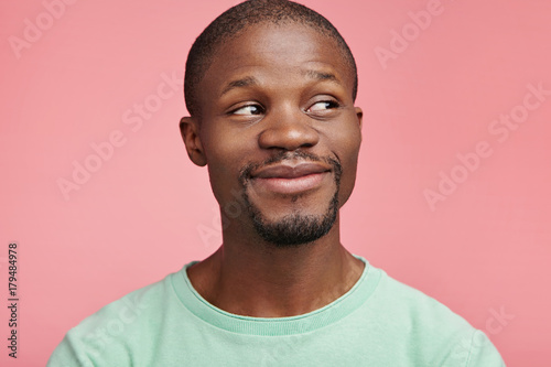Positive dreamy glad African American businessman looks happily and thoughtfully aside, thinks over business strategies, or dreams about good vacations with family and friends. Pleasure and people