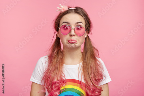 Offended coquette woman with pink tips of hair  curves lip  has quarrel with friend or boyfriend  has puzzled expression  looks resentfully into camera. People  fashion  beauty  style concept.