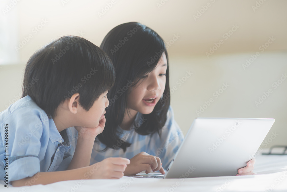 Asian children lying in bed and using laptop Asian children lying in bed and using laptop