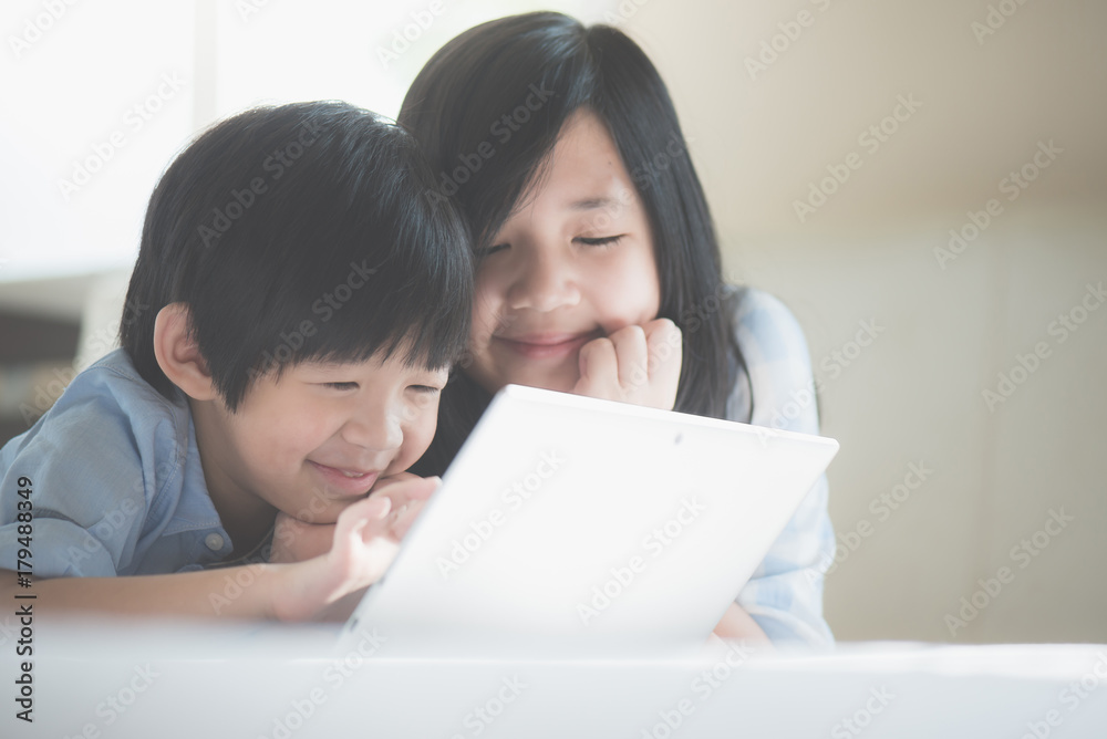 Asian children lying in bed and using laptop Asian children lying in bed and using laptop