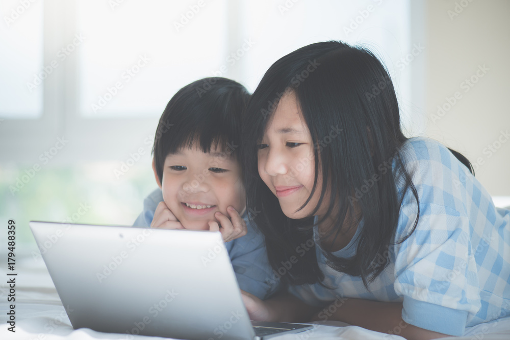 Asian children lying in bed and using laptop Asian children lying in bed and using laptop