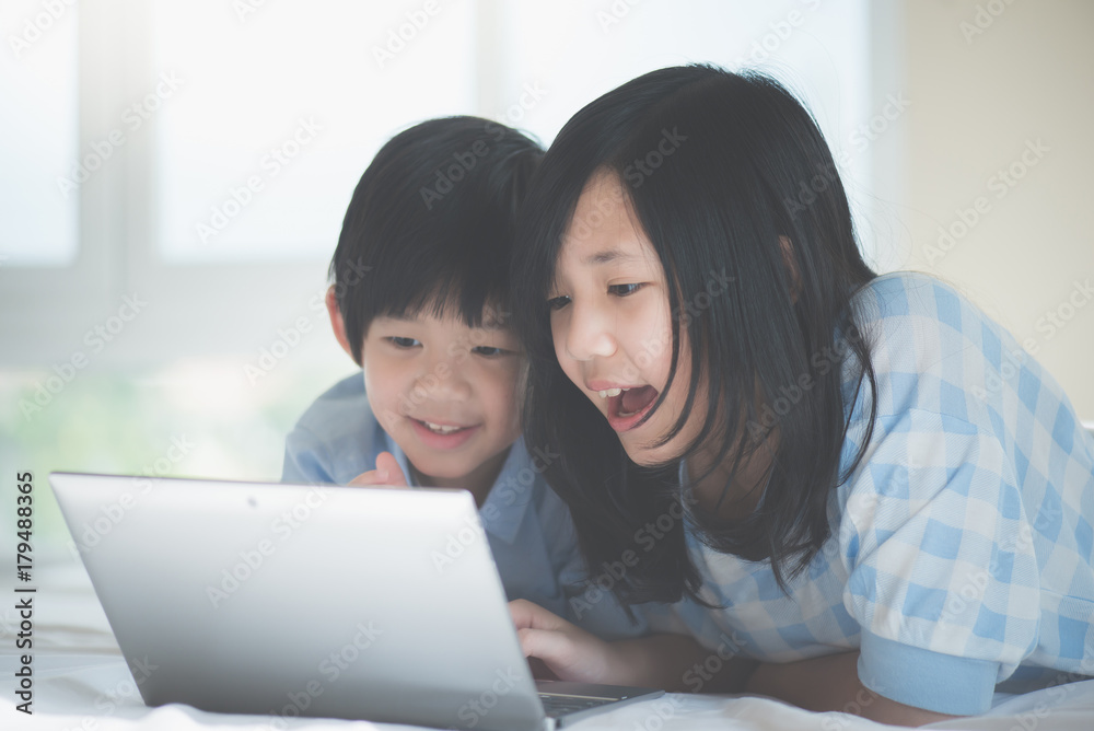 Asian children lying in bed and using laptop Asian children lying in bed and using laptop