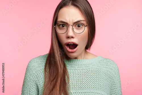 Astonished female brunette student opens mouth widely as find ou about putting forward exam on tomorrow, has no time for preparation, amazed by shocking news. Hush reaction and emotions concept