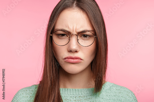 Close up portrait of discontent dissatisfied brunette female frowns face in dissatisfaction, being upset after quarrel with parents, doesn`t consider herself to be guilty. Unhappy embarrassed woman