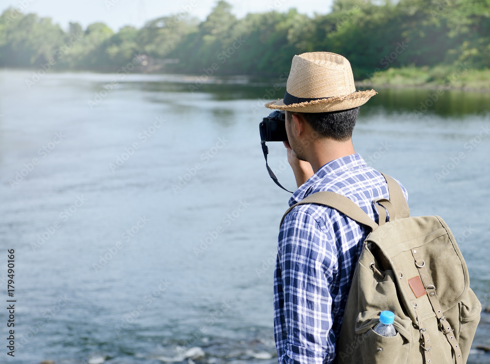 Young Asian tourist man with backpack looking thought the camera on river bank Young Asian tourist man with backpack looking thought the camera on river bank