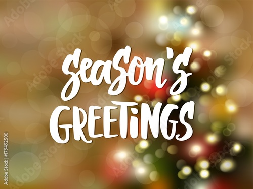 Season's greetings text, hand drawn lettering. Holiday greetings quote. Blurred background with Christmas tree and glowing lights. 