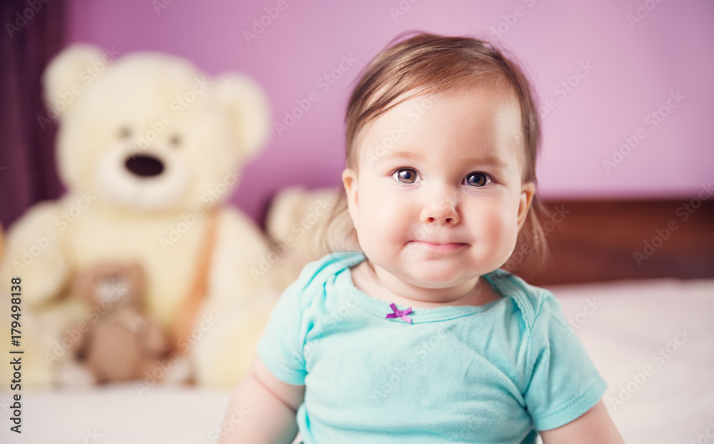Cute smiling little baby girl sitting on the bed with soft toys. Seven month old infant child on white soft blanket Cute smiling little baby girl sitting on the bed with soft toys. Seven month old infant child on white soft blanket