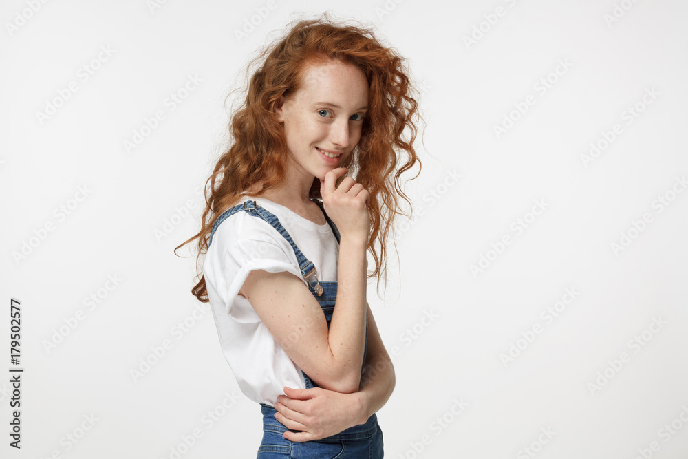 Indoor photo of young attractive European girl with red hair pictured isolated on white background turned to camera with right shoulder looking at interlocutor with attentive interested open smile Indoor photo of young attractive European girl with red hair pictured isolated on white background turned to camera with right shoulder looking at interlocutor with attentive interested open smile
