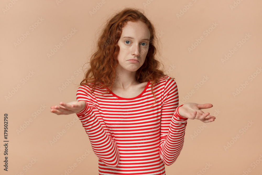 I don't know. Attractive young redhead student being at a loss, showing helpless gesture with arm and hands, mouth curved as if she does not know what to do