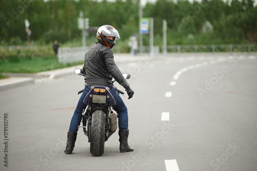 Sports, extreme, speed, adrenaline and determination concept. Rear view of stylish biker in leather clothes and safety helmet riding his motorcycle along empty high way, turning face to camera