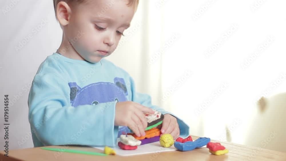 The child sculpts figures from plasticine sitting at the table at home