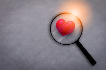 love concept with red heart object with magnifying glass on grey leather background