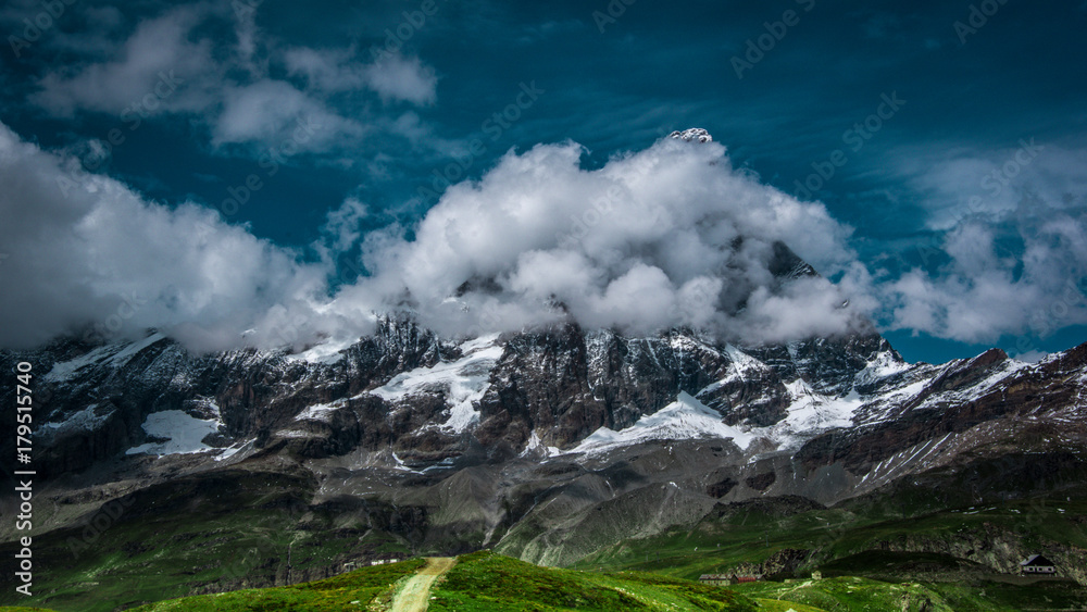 Landscape view of the south face of the Matterhorn, view from Plan Maison.Green meadow in the front, blue sky with white clouds above. Summer in the Pennine Alps, Valle d'Aosta, Italy, Europe.