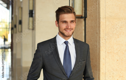 Portrait of happy young businessman standing in hotel lobby.