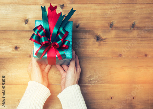 Creative hobby. Woman's hands wrap christmas holiday handmade present in craft paper with twine ribbon. Making bow gift box, decorated with cute object on wooden table, top view.