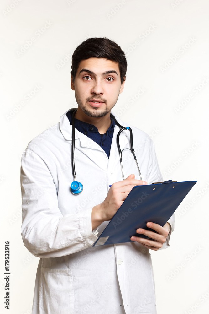 beautiful young doctor in a dressing gown with a stethoscope on a white background in the studio, records a medical history,