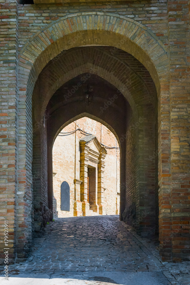 Brick arch, secondary entrance of Saludecio, a little medieval town in the Montefeltro, in the Emilia Romagna region, between Rimini and Urbino. The door of a church appears in the background