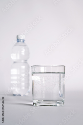 un bicchiere trasparente pieno di acqua. vicino una bottiglia di acqua minerale. composizione con bottiglie di acqua minerale
