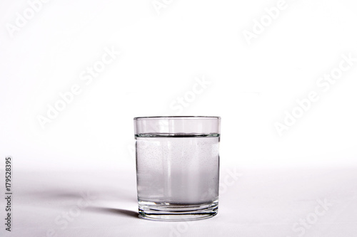 un bicchiere  trasparente pieno di acqua. vicino una bottiglia di acqua minerale. composizione con bottiglie di acqua minerale