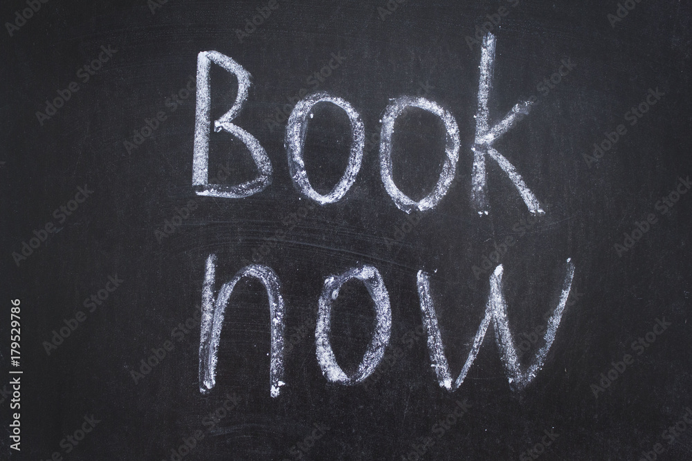 Fototapeta premium Text Book Now handwritten with white chalk on a blackboard. 