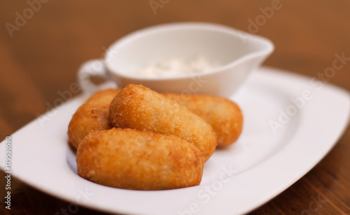 Potato croquettes with jamon and white saucepan in white plate. Brown blurred background. Selective soft focus photography