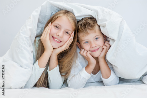 Two happy sibling children lying under blanket