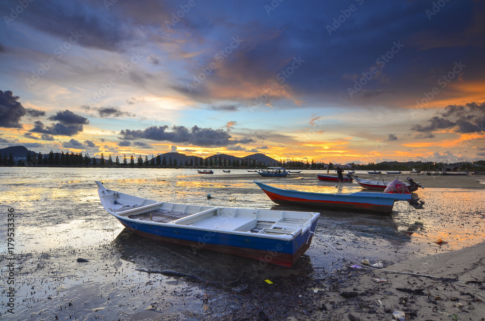 Fisherman boat on mud during lowtide with dramatic sunset at background.