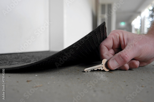 Man picking up or hiding a key under the door mat
