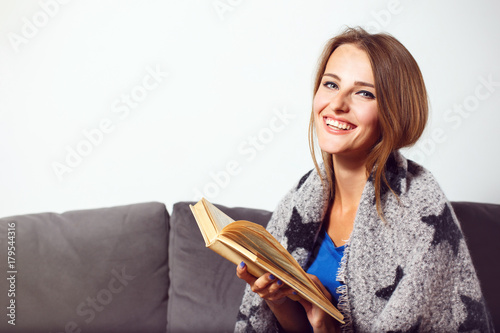 Cheerful girl sitting in armchair with plaid and glass of tea before bricks wall photo