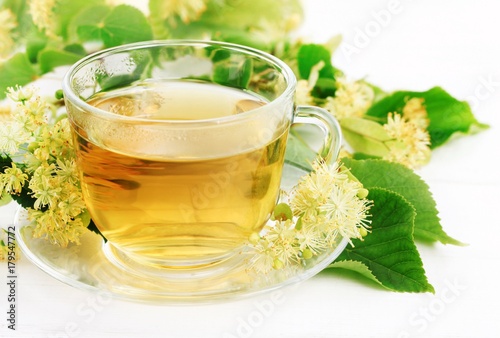 Glass cup of herbal linden tea with fresh green lime tree leaves and yellow blossom. Tasty and healthy drink. 