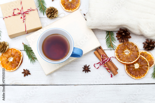 A cup of hot tea is on the book, and around the Christmas decorations on a wooden background. Flat lay
