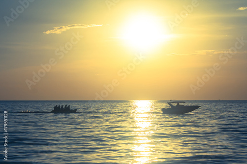 Silhouette of people playing banana boat on the sea with beautiful view of sunset light in the background at Chao Lao Beach, Chanthaburi Province, Thailand.