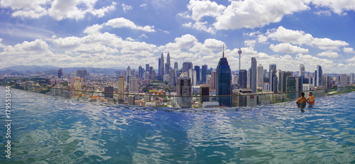 Canvas Print Unidentified businessman and traveller swimming in infinity pool with Kuala Lumpur City skyline and dramatic cloud formation at background