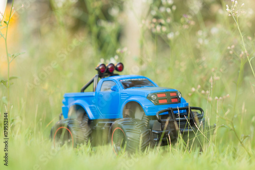 A scene of Blue RC Off-road truck car (Radio-controlled) is parked on the green grass with blurred meadow background. (This toy has some dust from children playing)