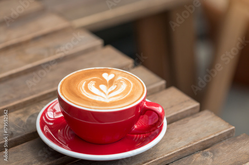 A red cup of hot latte coffee with latte art on the wooden table background.
