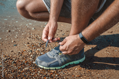 male athlete tying sports shoe at the seashore in summer