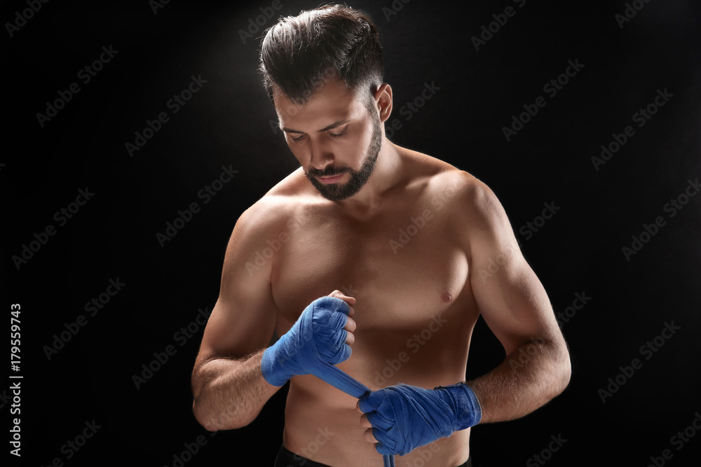 Male boxer applying wrist wraps on dark background Male boxer applying wrist wraps on dark background