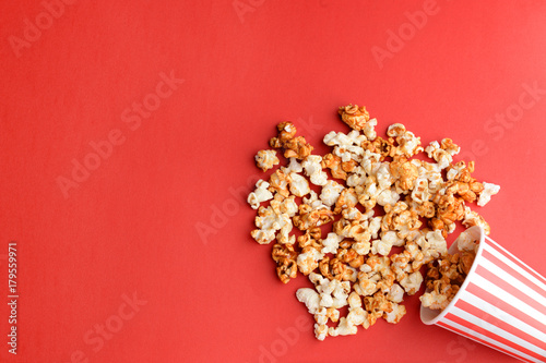Overturned cup with tasty caramel popcorn on color background