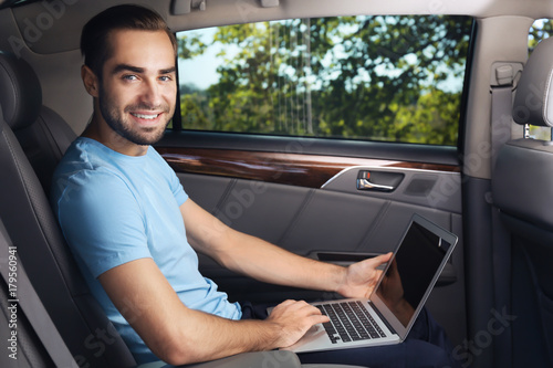 Young man with laptop on backseat of car © Africa Studio