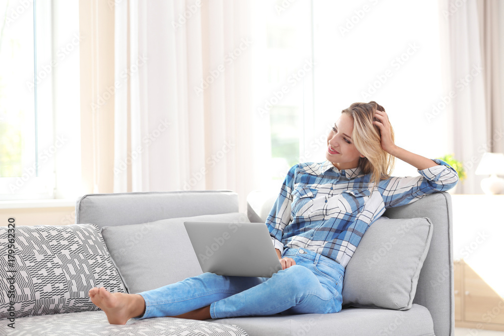 Beautiful young woman with modern laptop on sofa at home Beautiful young woman with modern laptop on sofa at home