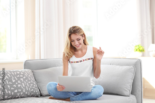 Beautiful young woman with modern laptop on sofa at home